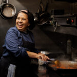 A photo of a woman cooking curry in a large pan on a hob - photography competition submission