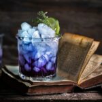 A photo of a vibrant deep blue and purple cocktail in a glass, placed on the worn pages of an old book - photography competition submission