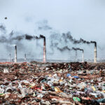 A photo of a large waste site filled with discarded food, with chimneys releasing black smoke in the background - photography competition submission
