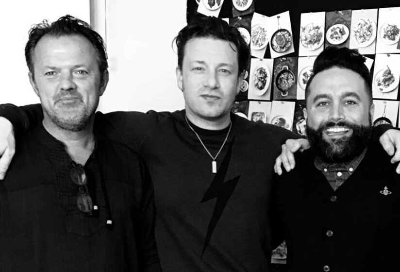A black and white photo of Jamie Oliver, James Verity and David Loftus holding arms round each other and smiling