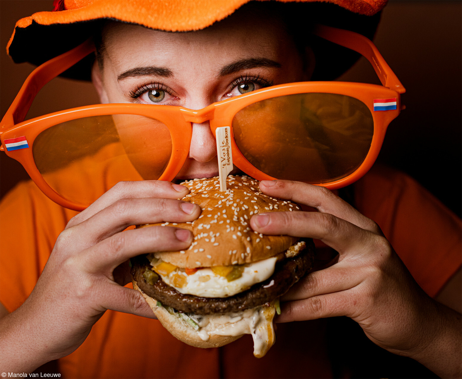 a women wearing orange eating a big juicy burger
