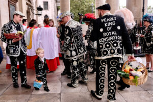 A photo of people, including a young boy, in pearl-adorned outfits carrying food baskets at the London Pearly Kings & Queens Harvest Festival